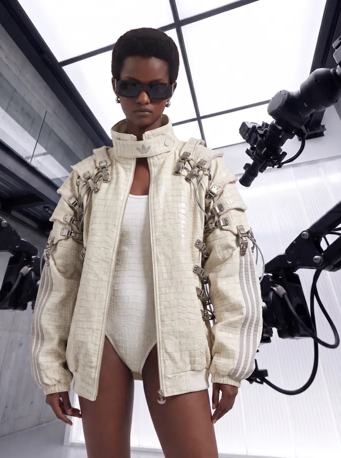 Modelo con chaqueta de piel blanca con hebillas metálicas rodeada de brazos robóticos